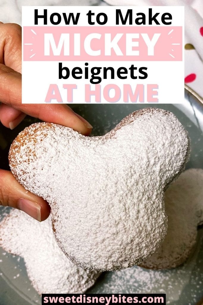 a hand holding a Mickey beignet on a plate topped with powdered sugar